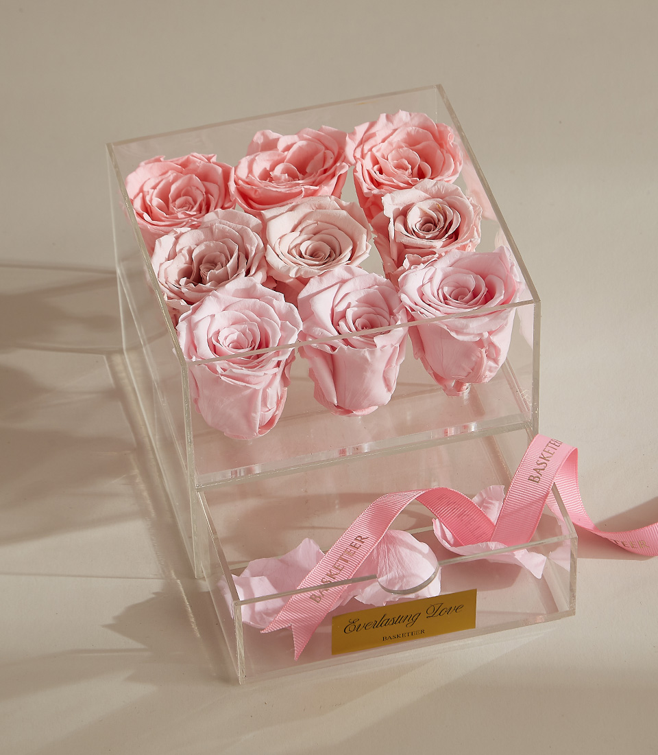 A luxury preserved rose arrangement featuring nine pink roses in a clear acrylic box with a keepsake drawer and elegant pink ribbon.
