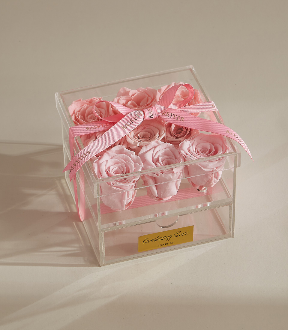 A luxury preserved rose arrangement featuring nine pink roses in a clear acrylic box with a keepsake drawer and elegant pink ribbon.