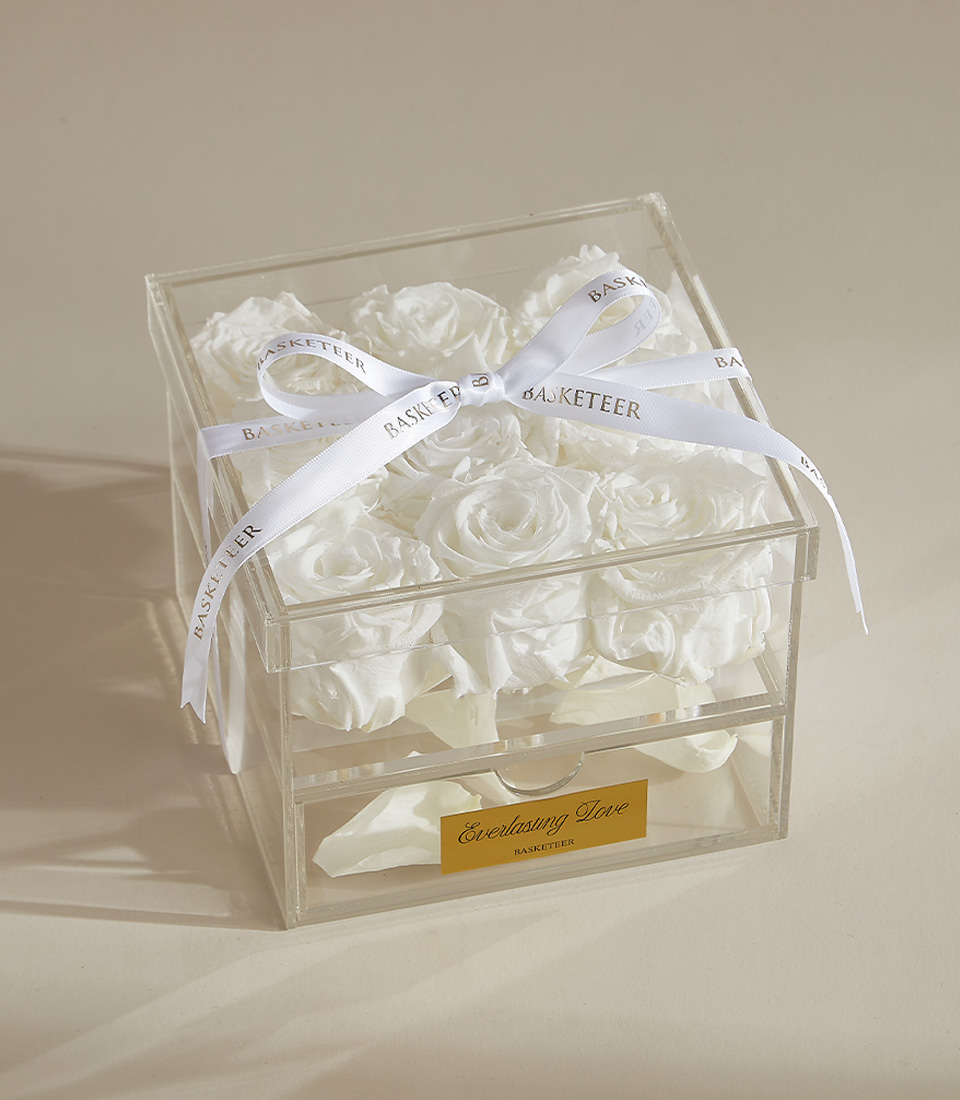 A luxurious preserved white rose arrangement featuring nine elegant roses in a clear acrylic box with a keepsake drawer, tied with a white ribbon.