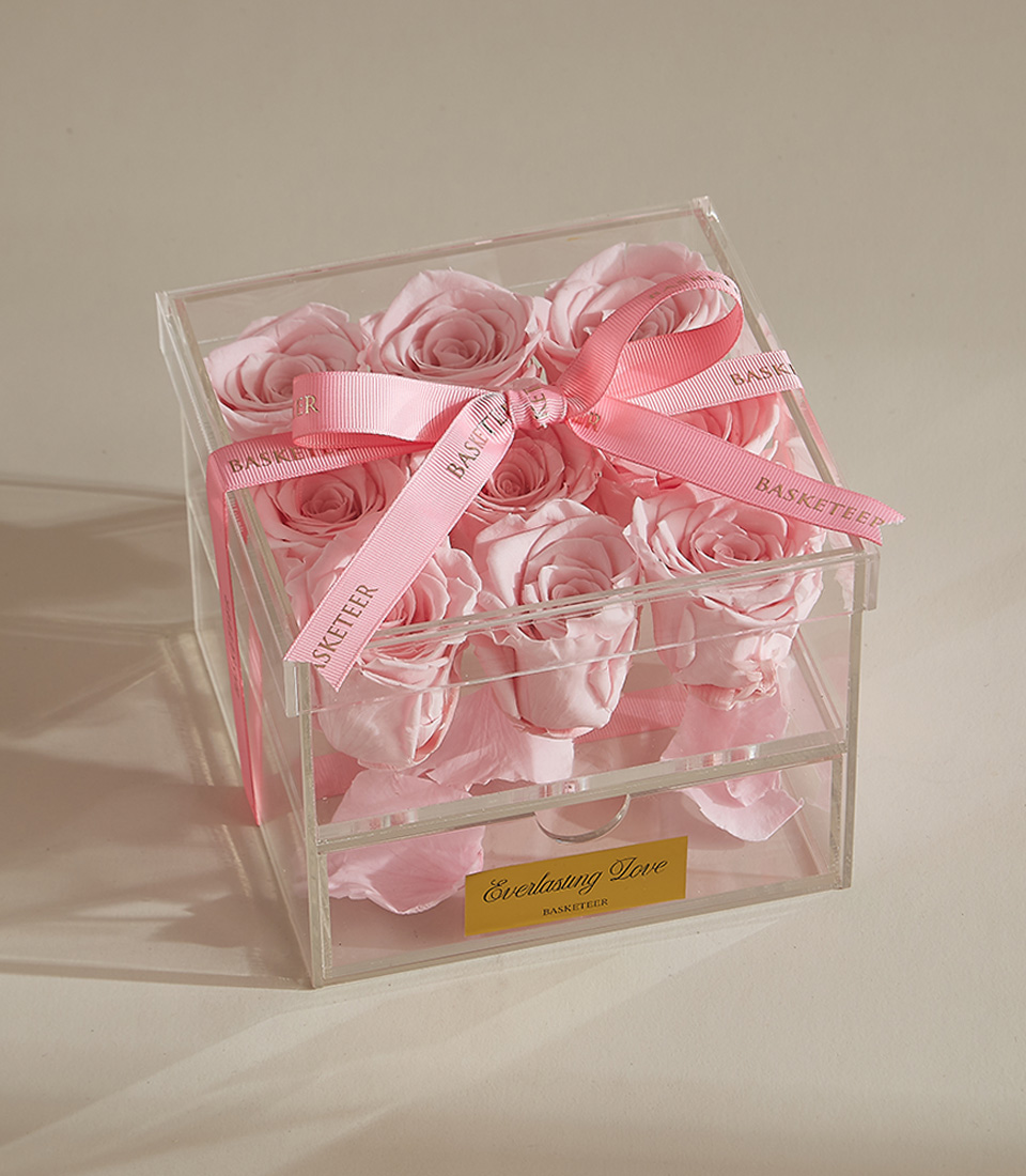 A luxury preserved rose arrangement featuring nine pink roses in a clear acrylic box with a keepsake drawer and elegant pink ribbon.