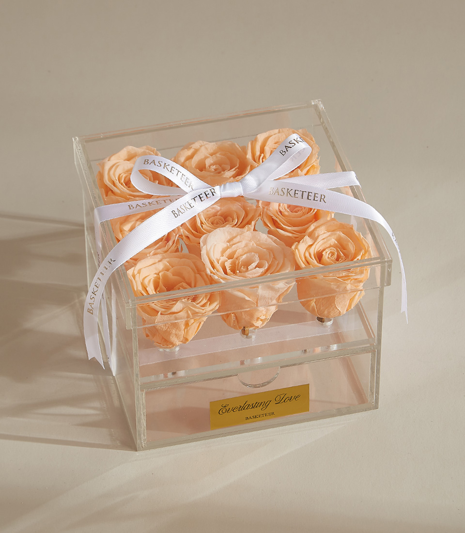 A beautiful preserved peach rose arrangement featuring nine roses in a luxury acrylic box with a keepsake drawer, finished with a white ribbon.