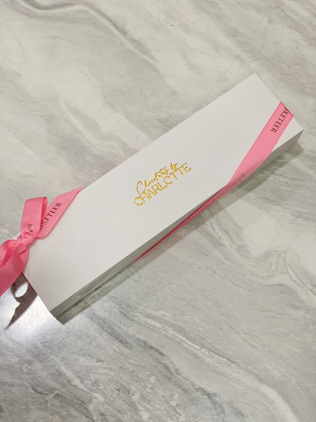 A luxurious white chocolate gift box with gold foil branding, wrapped with a pink satin ribbon, perfect for gifting.