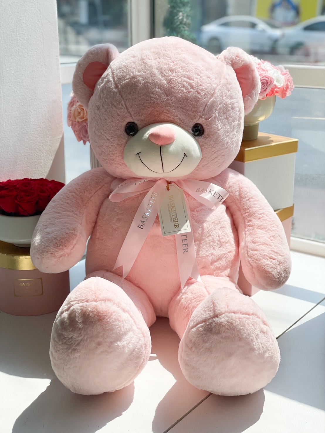 A giant pink plush teddy bear with a Basketeer ribbon and tag, perfect for Valentine’s gifts, birthdays, and romantic surprises.