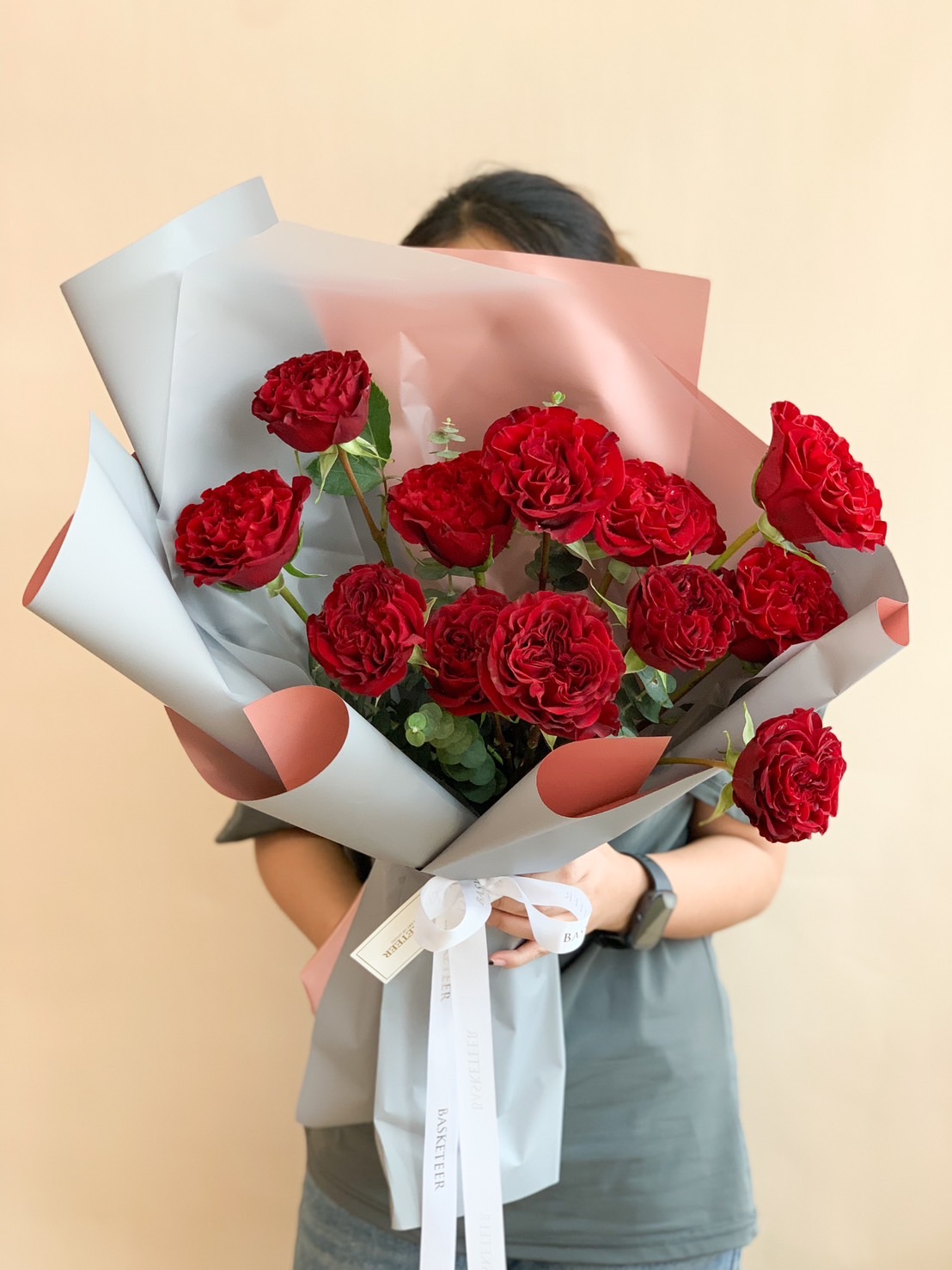 A beautifully hand-tied bouquet of rich red roses, elegantly wrapped in white and blush-toned paper with a soft white ribbon, creating a classic and timeless floral arrangement.