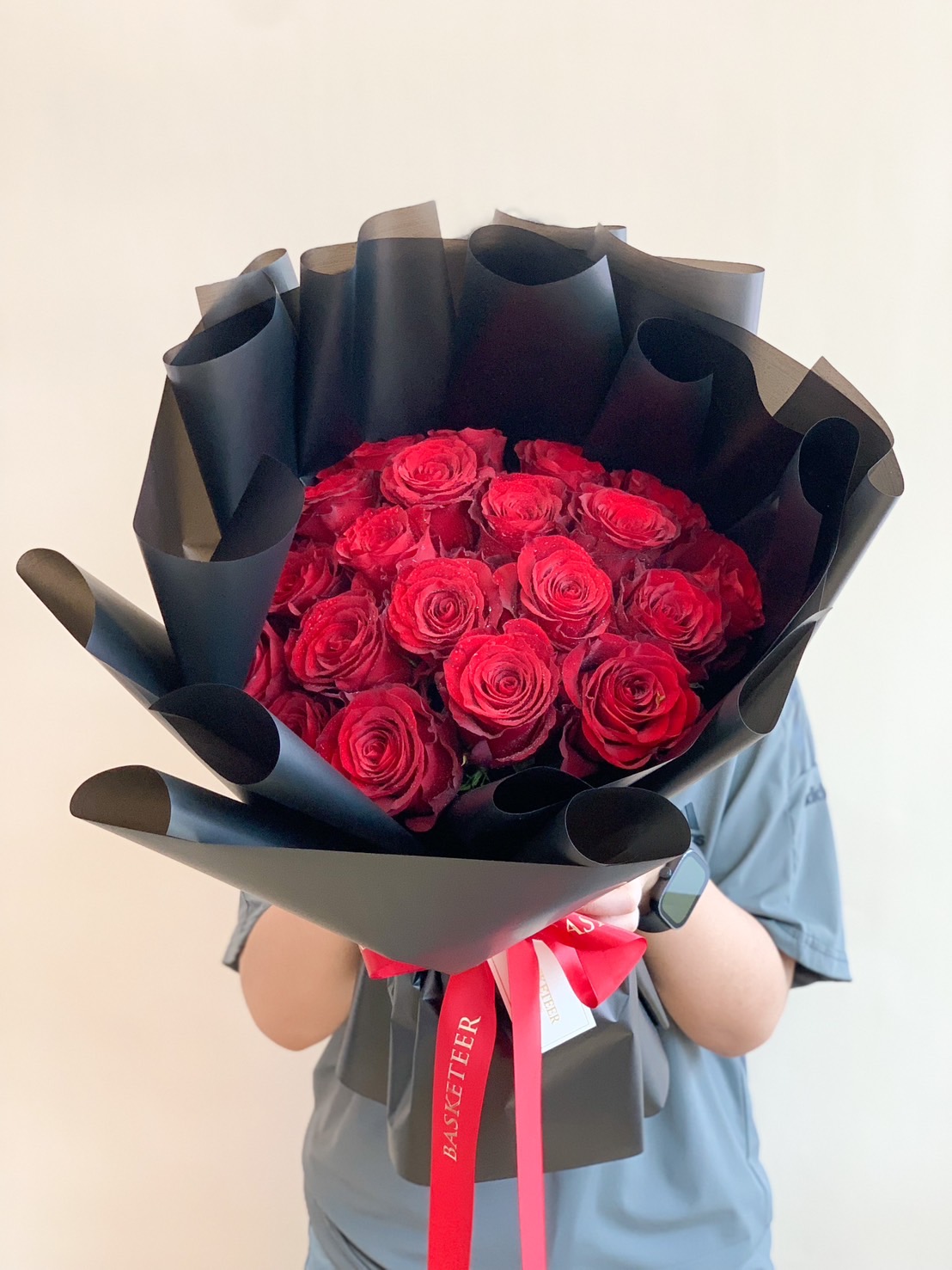 A luxurious bouquet of deep red roses wrapped in elegant black paper, tied with a Basketeer ribbon, perfect for romantic gifts and special occasions.