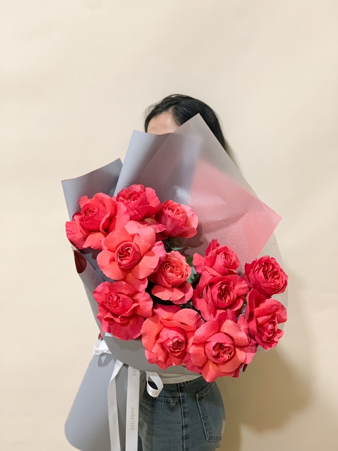 A beautifully hand-tied bouquet of rich red roses, elegantly wrapped in white and blush-toned paper with a soft white ribbon, creating a classic and timeless floral arrangement.