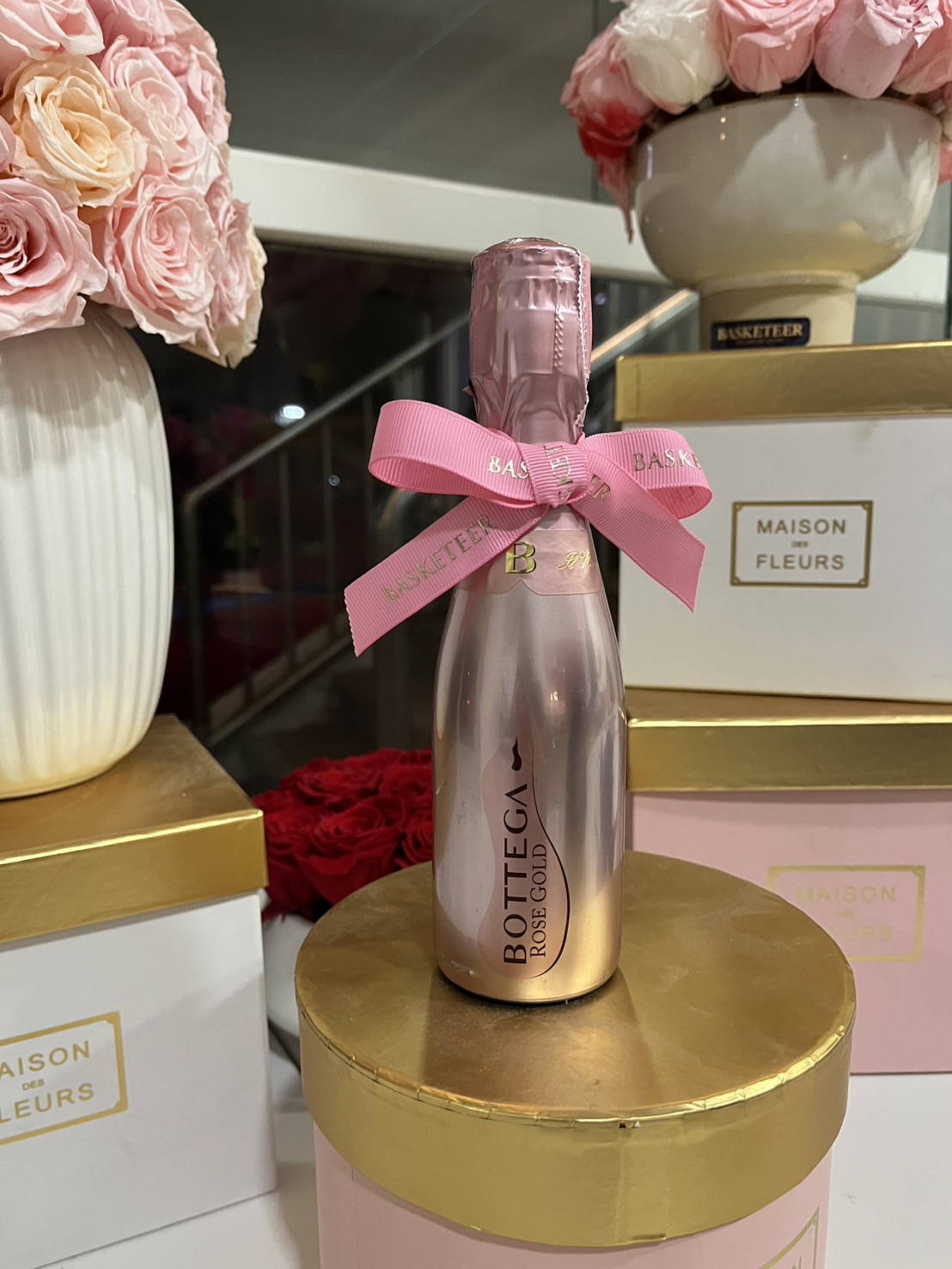 A mini bottle of Bottega Rose Gold sparkling wine, elegantly wrapped with a pink ribbon, placed on a luxury gold and pink gift box. Meta Description: