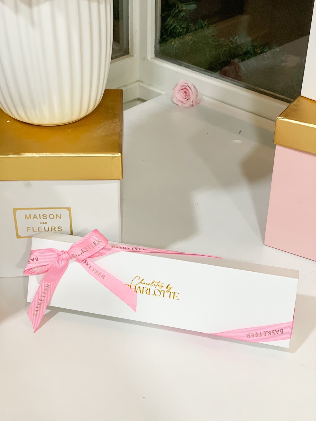 A luxurious white chocolate gift box with gold foil branding, wrapped with a pink satin ribbon, perfect for gifting.