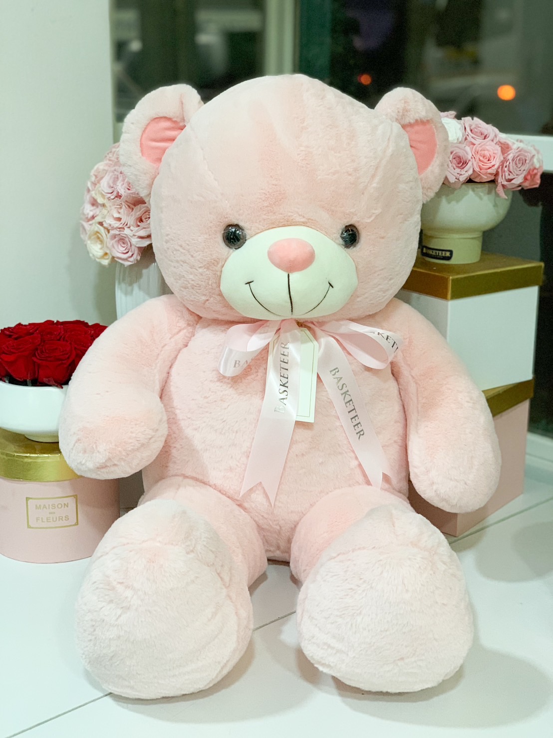 A giant pink plush teddy bear with a Basketeer ribbon and tag, perfect for Valentine’s gifts, birthdays, and romantic surprises.