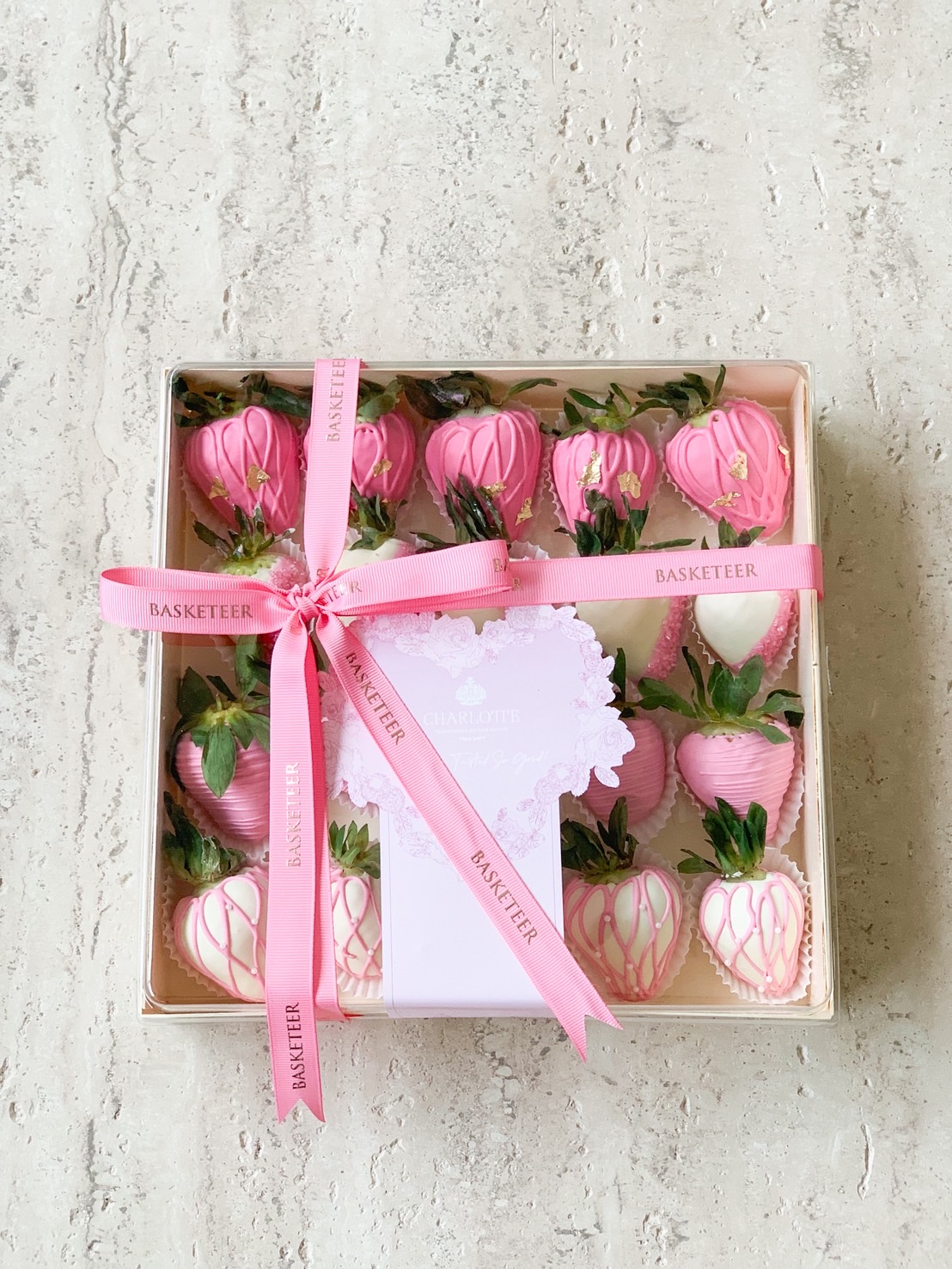 Gift box of pink and white chocolate-dipped strawberries, tied with a pink ribbon and decorated with edible gold flakes.
