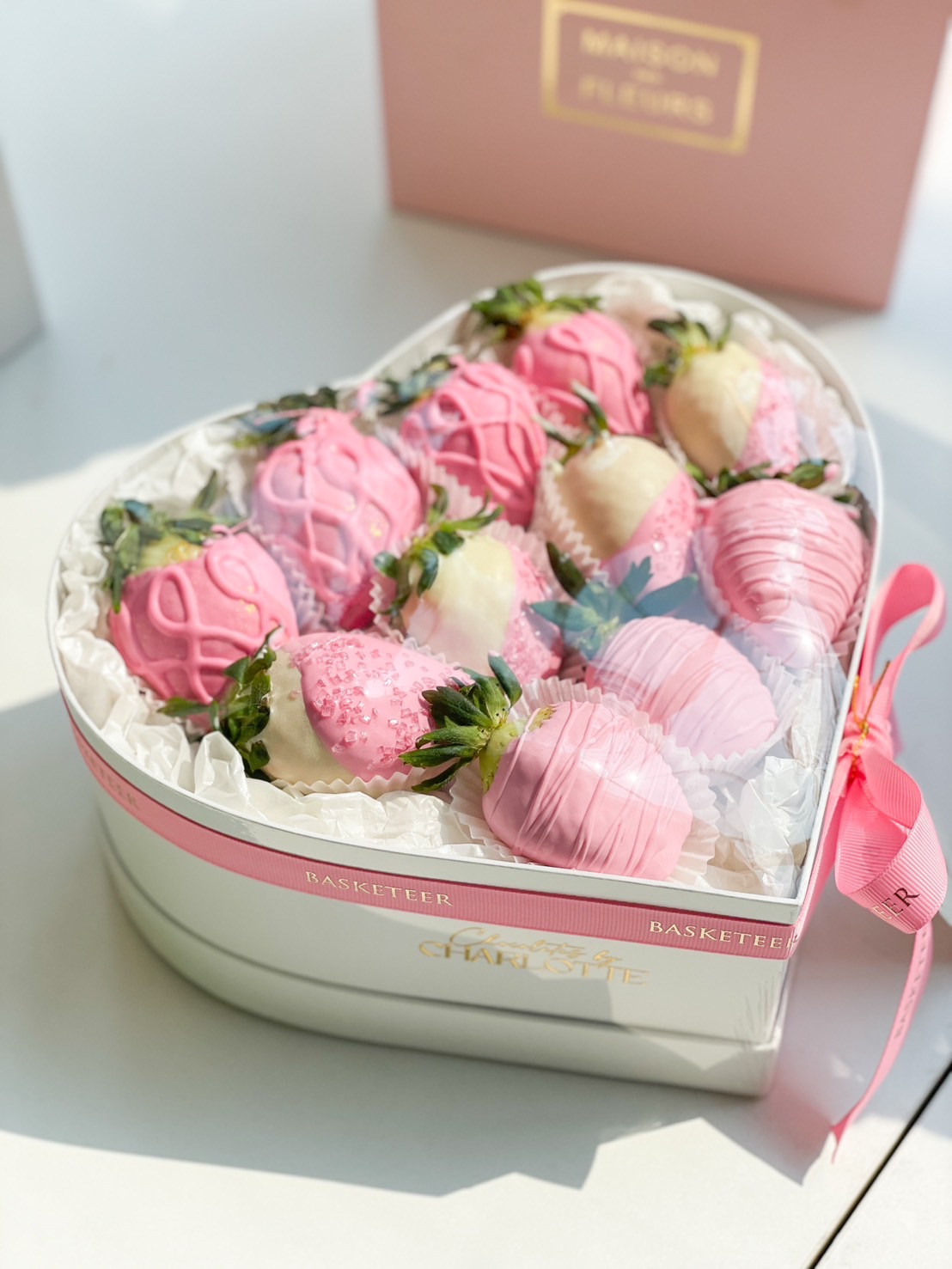 Heart-shaped box of pink and white chocolate-covered strawberries with gold accents, sugar crystals, and delicate drizzles.
