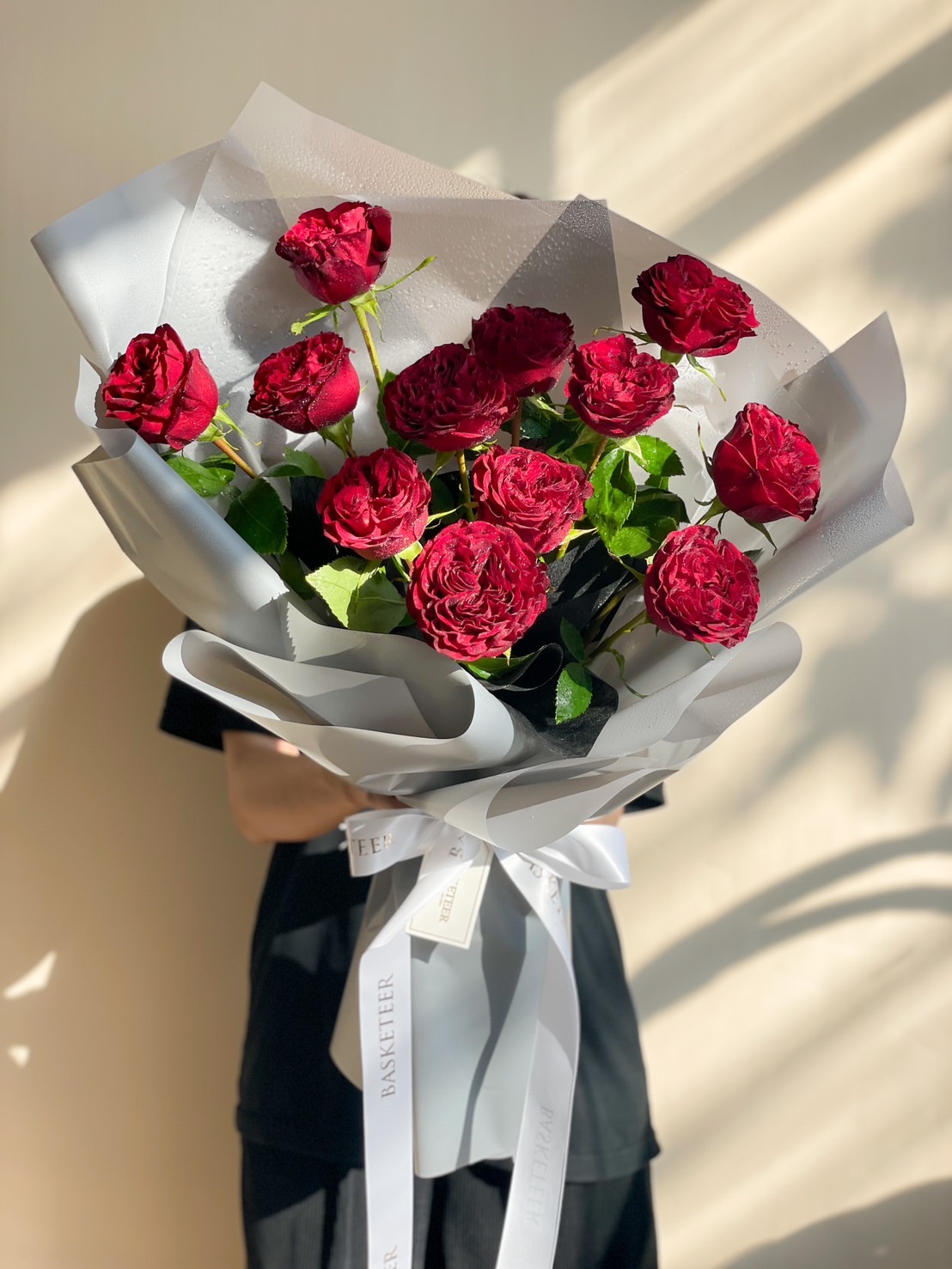 A stunning bouquet of deep red velvet roses, elegantly wrapped in soft grey paper with a white ribbon, symbolizing love and romance.