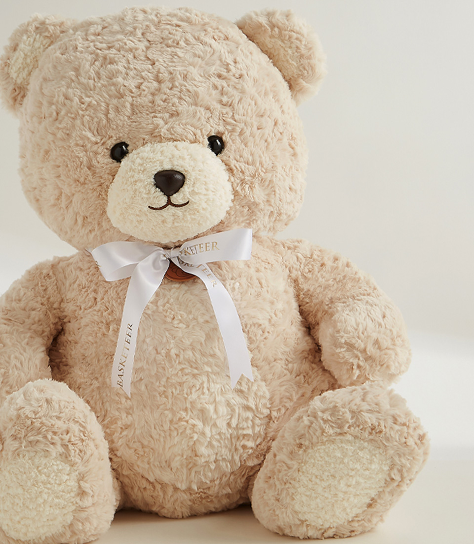 Large beige plush teddy bear with a white ribbon, soft and huggable, perfect for gifts, snuggles, and special occasions.