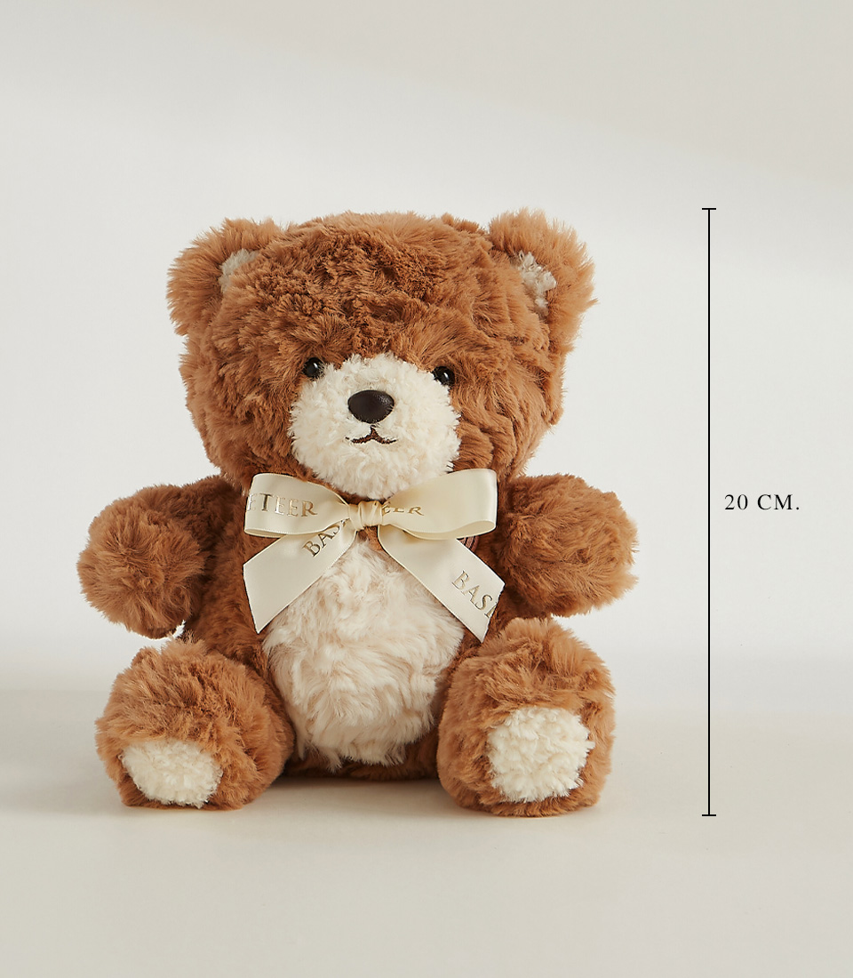 Brown and white plush teddy bear with a cream ribbon around its neck, seated upright on a neutral background. A vertical line with 