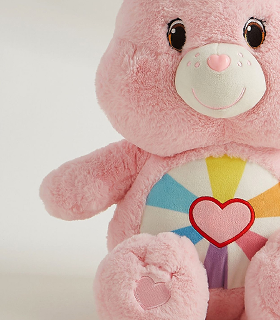 A cute pink plush bear with a rainbow heart design on its belly, soft fur, embroidered heart-shaped paws, and a sweet smile.