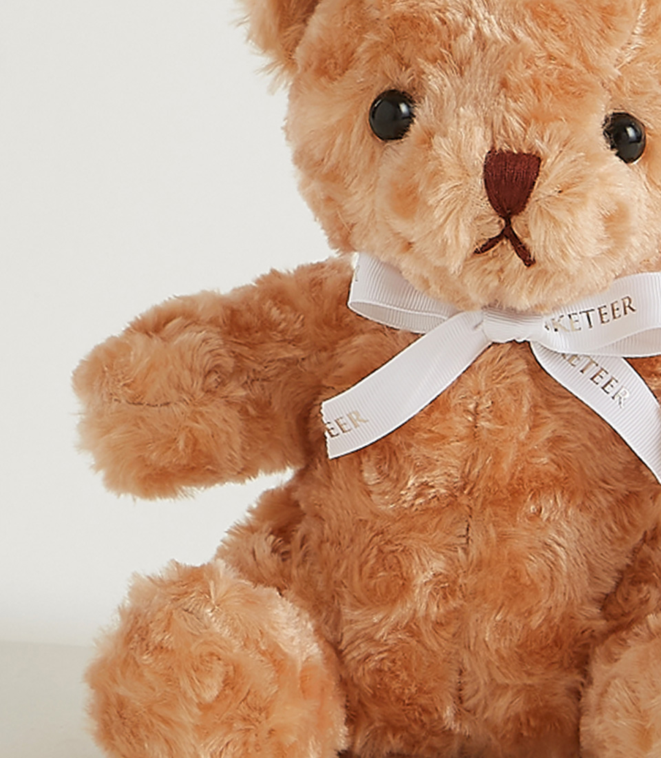 Small caramel-colored plush teddy bear with a white ribbon, soft and cuddly, perfect for gifting and snuggling.
