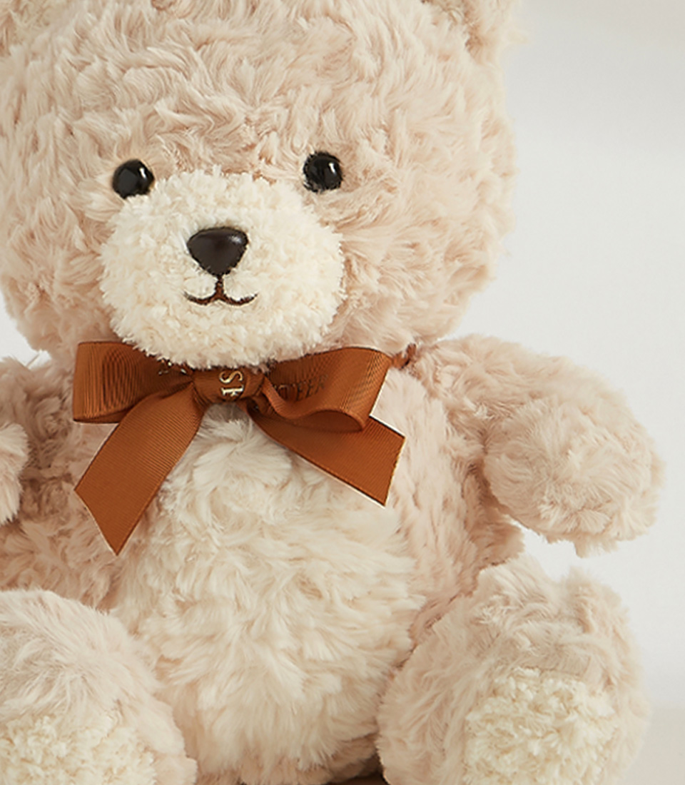 Soft beige teddy bear with a brown bow, featuring a plush and cuddly design, perfect for gifting and cozy snuggles.