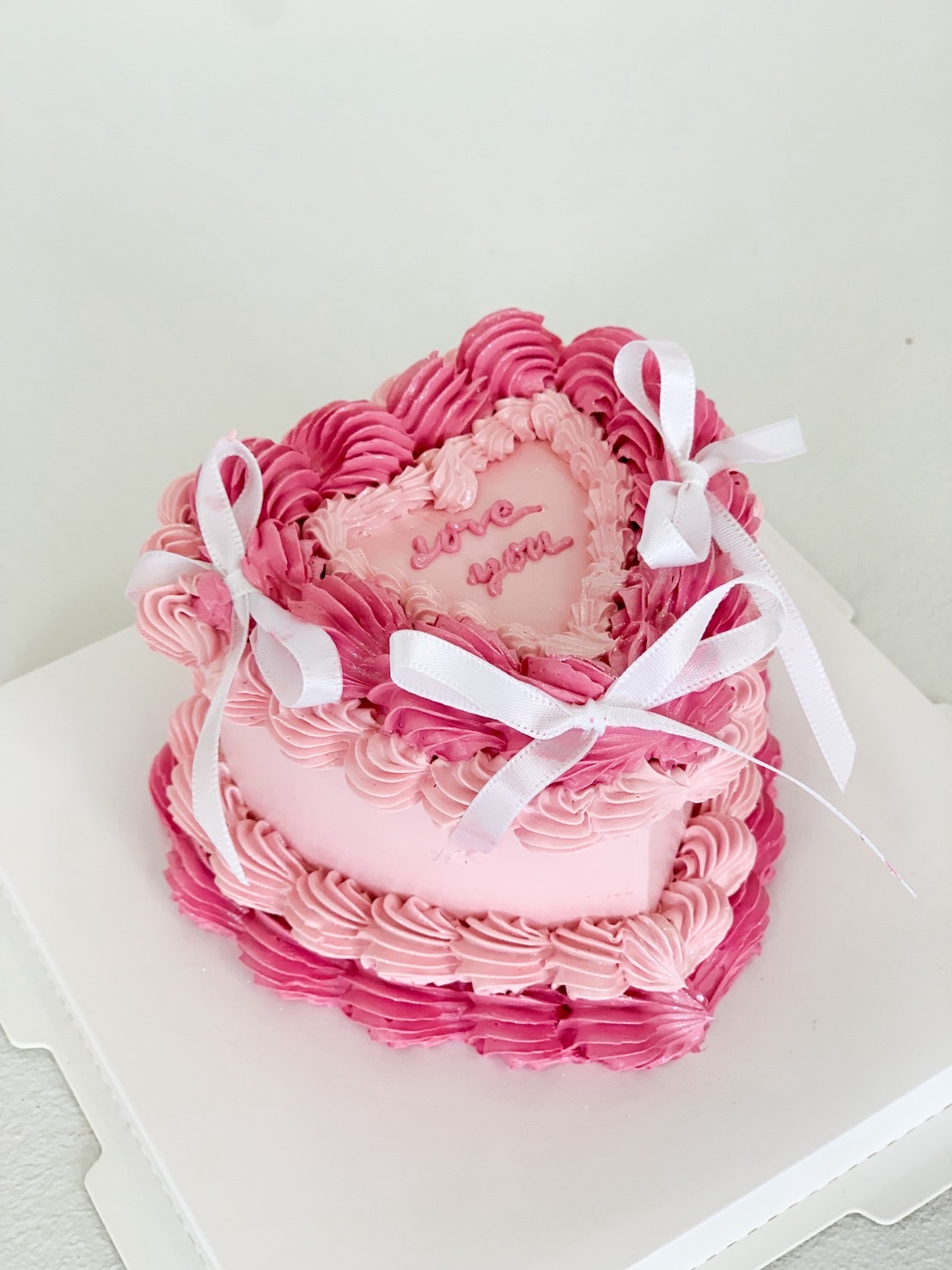 Pink heart-shaped vintage cake with white ribbon details, pink swirl frosting, and 