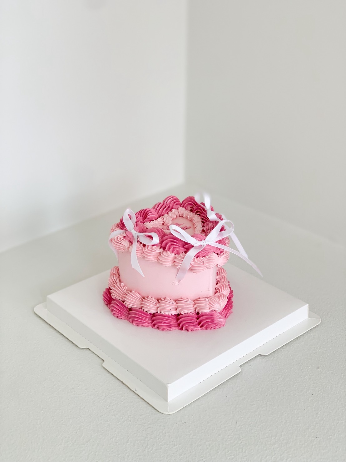 Pink heart-shaped vintage cake decorated with pink frosting swirls and white satin ribbons, no message