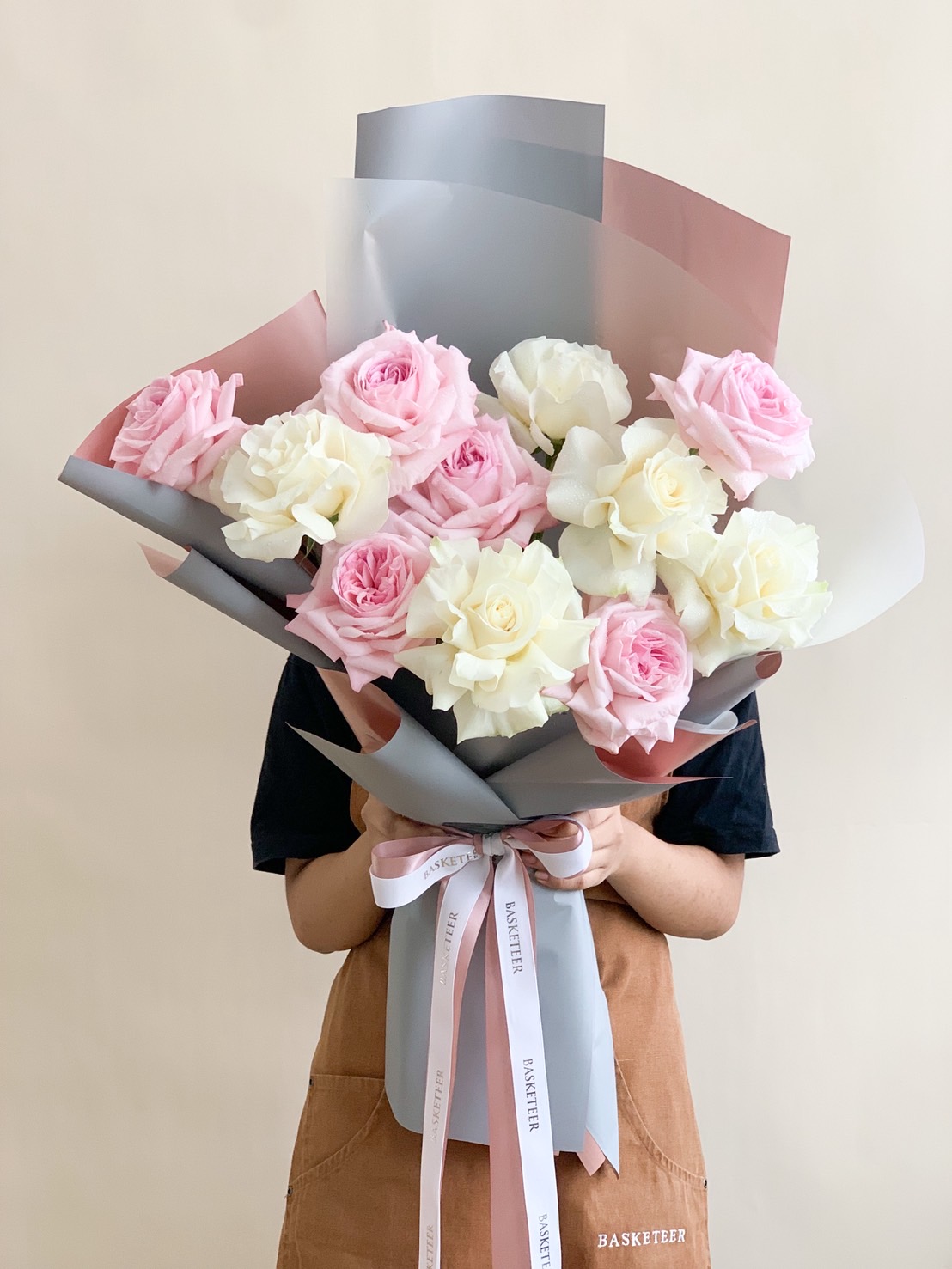 Handheld bouquet of soft pink and white roses wrapped in pastel paper with a satin ribbon, perfect for romantic occasions.