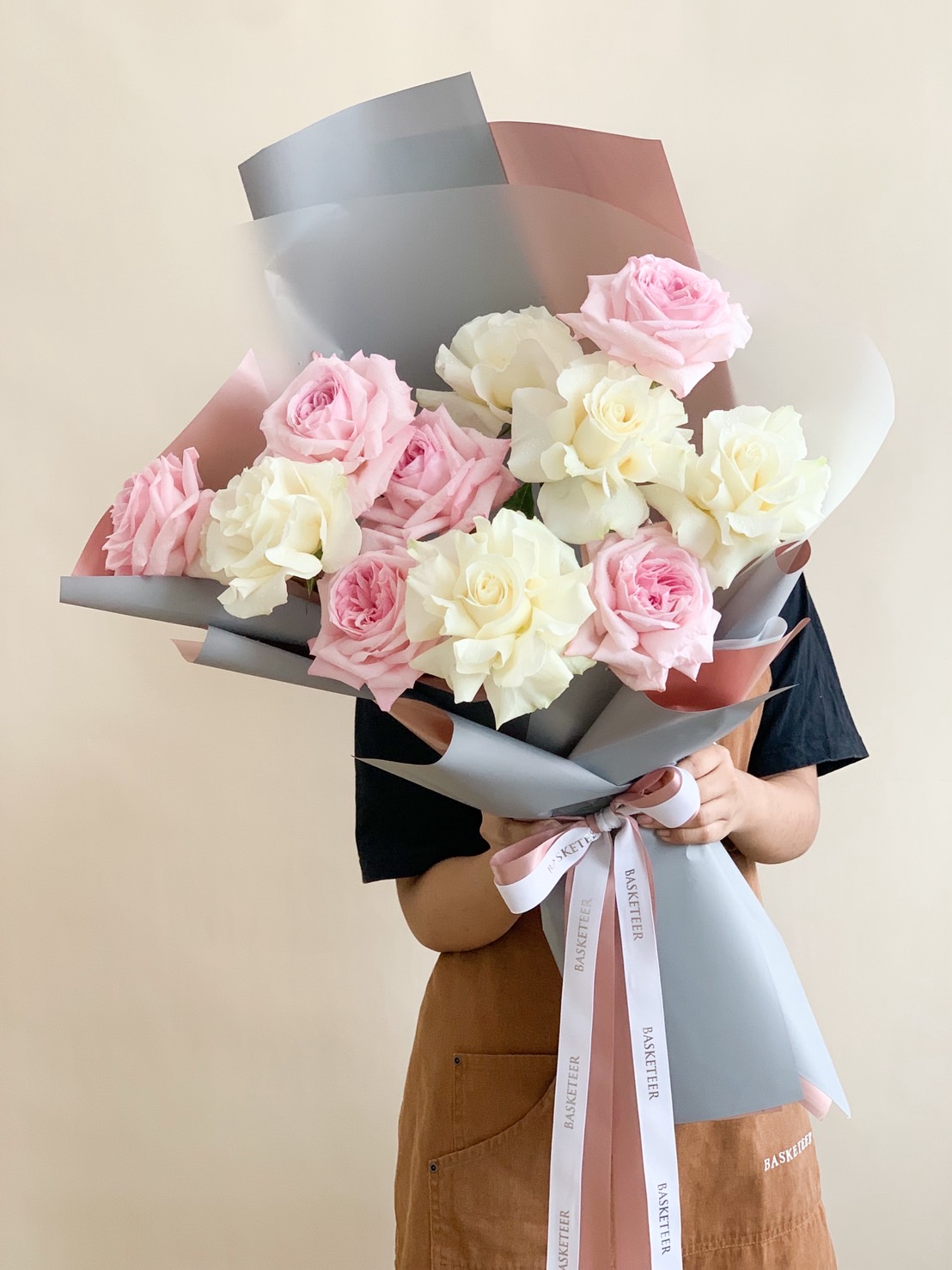 Handheld bouquet of soft pink and white roses wrapped in pastel paper with a satin ribbon, perfect for romantic occasions.