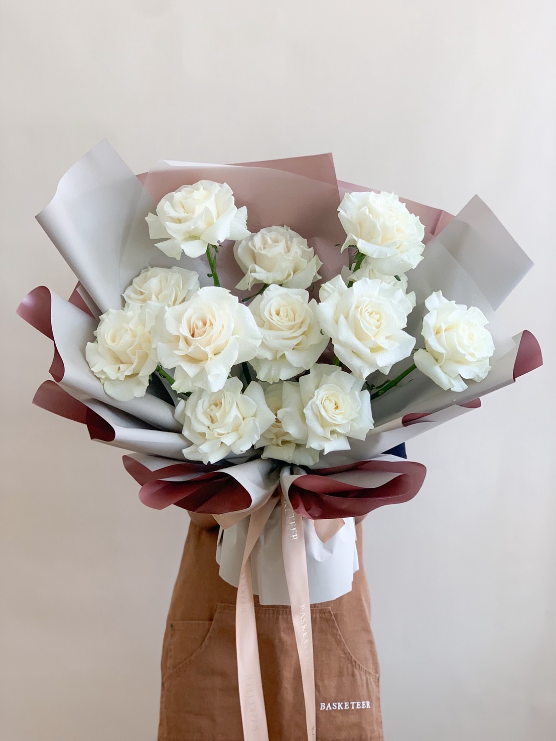 A bouquet of elegant white roses wrapped in soft-toned paper and tied with satin ribbons, perfect for weddings, sympathy, or serene celebrations.