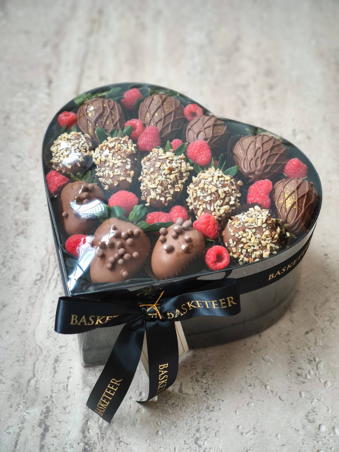 Heart-shaped box with chocolate-dipped strawberries, fresh raspberries, and assorted toppings tied with black satin ribbon