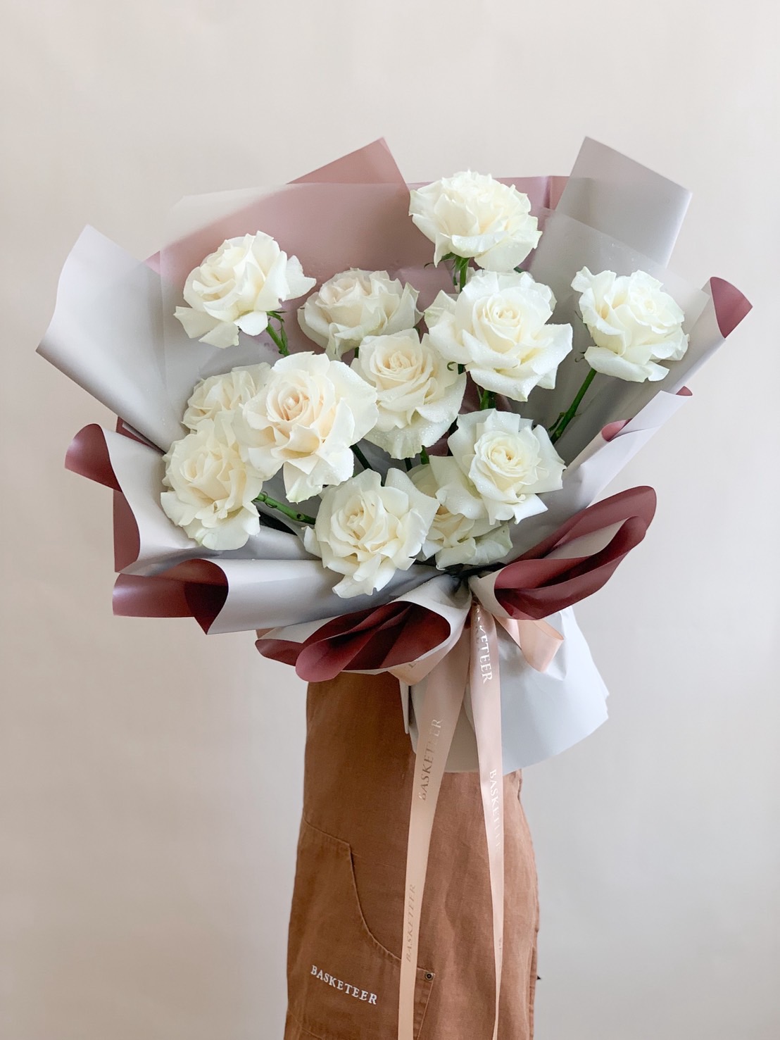 A bouquet of elegant white roses wrapped in soft-toned paper and tied with satin ribbons, perfect for weddings, sympathy, or serene celebrations.