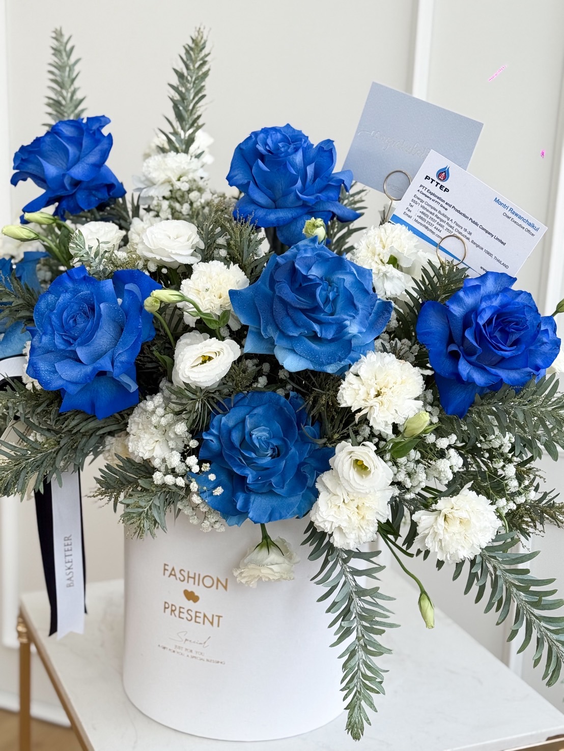 Luxury round box with blue roses, white roses, lisianthus, gypsophila, and greenery, designed as an elegant congratulatory arrangement.