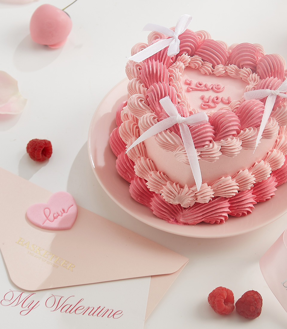 Close-up of a beautiful pink heart-shaped cake with piped buttercream swirls, white bows, and 