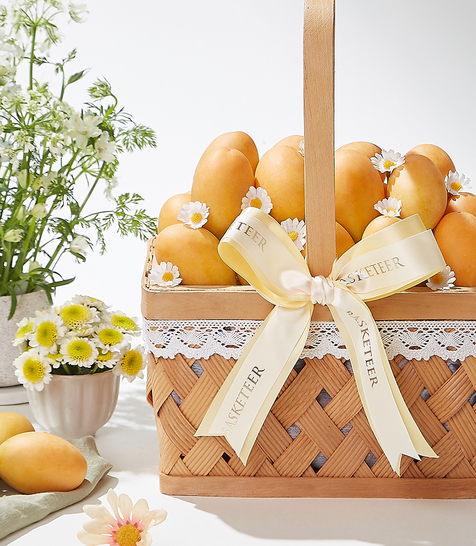 A beautifully handcrafted woven basket filled with premium Mayongchid (Marian Plum) fruit, elegantly decorated with a satin ribbon, exuding sweet tropical flavors and a delicate aroma.