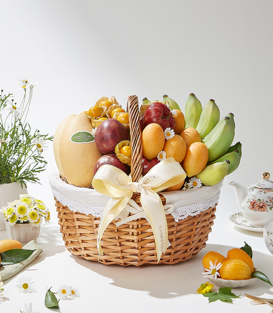 A wicker basket filled with premium Mayongchids from Nakhon Nayok, Nam Dok Mai See Thong mangoes from Chachoengsao, passion fruits, rose apples, Ducasse bananas, and cape gooseberries elegantly decorated with a cream ribbon and lace