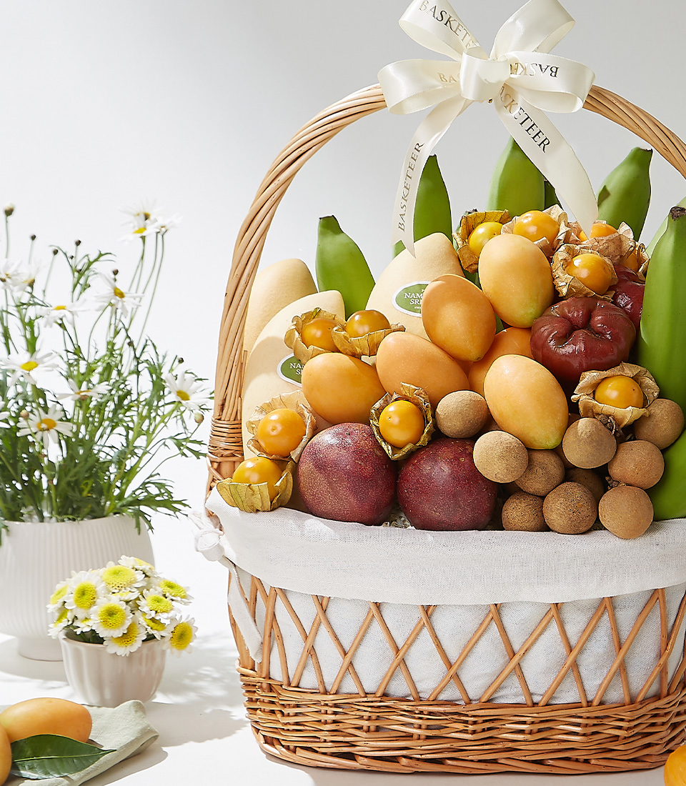 A wicker basket filled with premium Mayongchids from Nakhon Nayok, Nam Dok Mai See Thong mangoes, passion fruits, rose apples, green Cavendish bananas, longans, and cape gooseberries elegantly arranged with a white ribbon