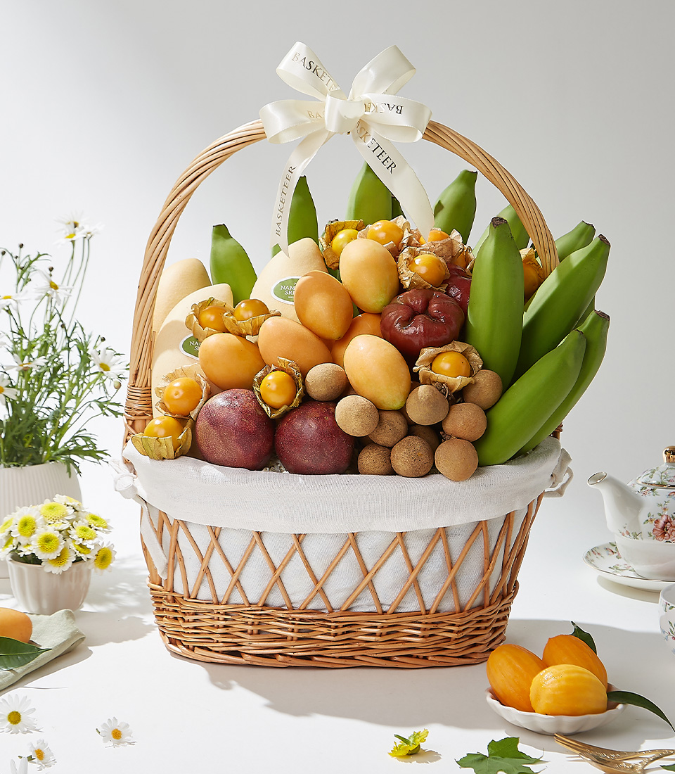 A wicker basket filled with premium Mayongchids from Nakhon Nayok, Nam Dok Mai See Thong mangoes, passion fruits, rose apples, green Cavendish bananas, longans, and cape gooseberries elegantly arranged with a white ribbon
