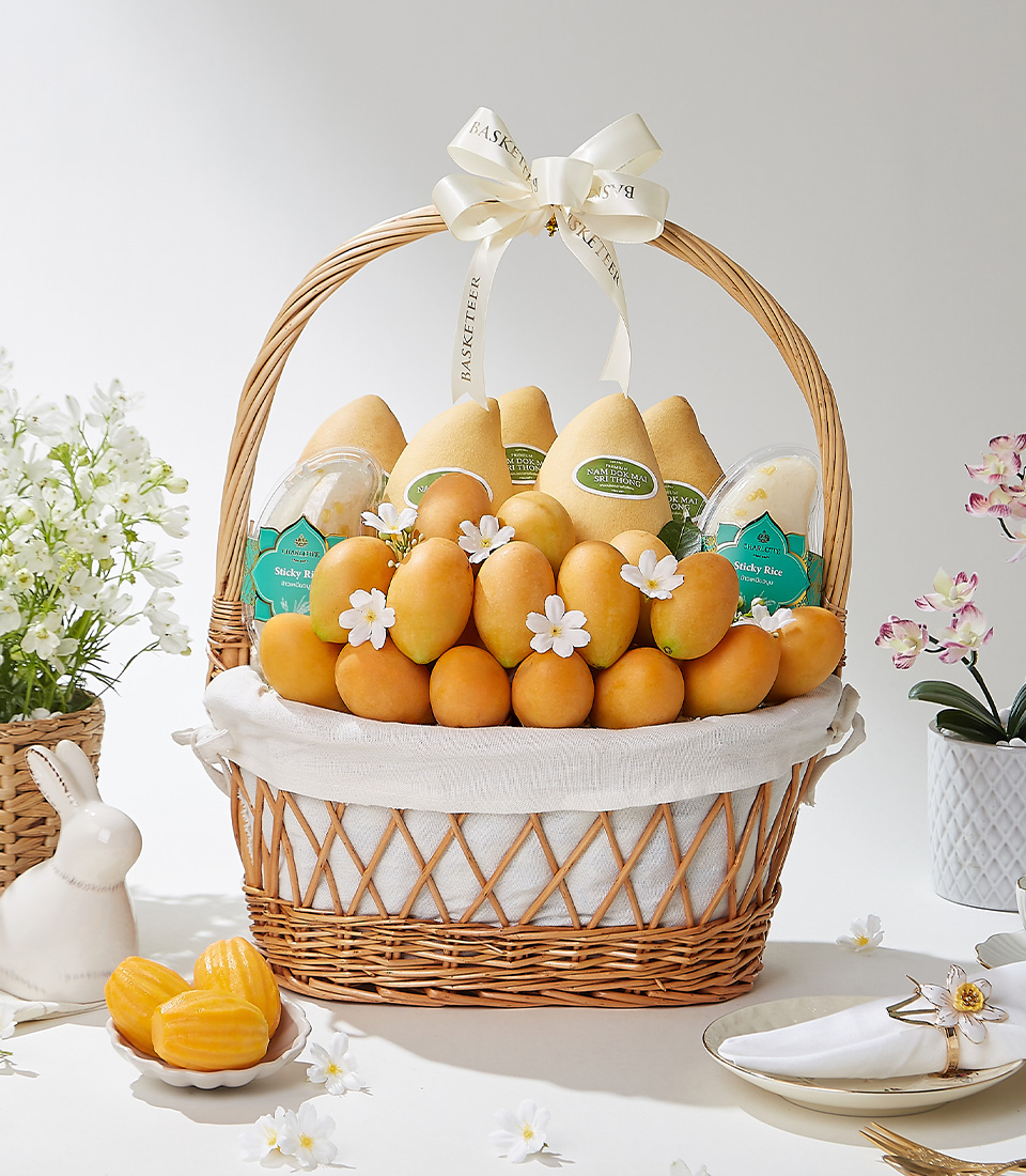 A wicker basket filled with 1.5 kg of premium Mayongchids from Nakhon Nayok, Nam Dok Mai See Thong mangoes from Chachoengsao, and Snow Pearl sticky rice, elegantly decorated with white flowers and a cream ribbon