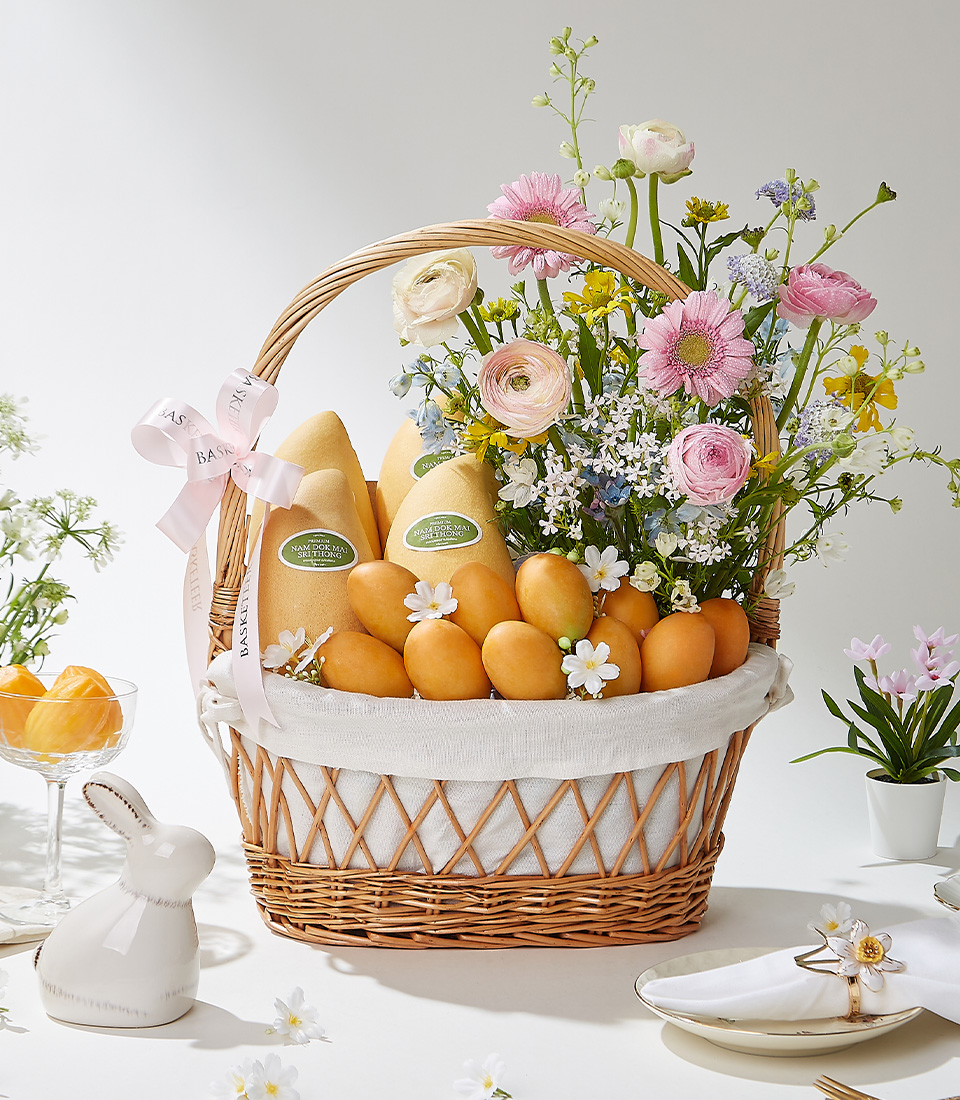 A Rustic Elegance wicker basket filled with 1 kg of premium Mayongchids from Nakhon Nayok, Nam Dok Mai See Thong mangoes, and beautifully arranged fresh flowers, elegantly decorated with a pink ribbon