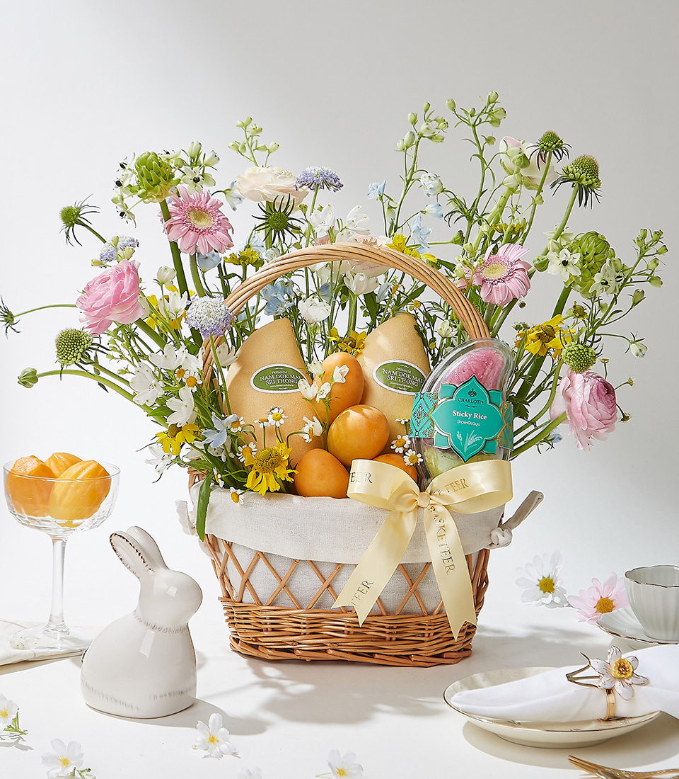 A Rustic Elegance wicker basket filled with 0.3 kg of premium Mayongchids from Nakhon Nayok, Nam Dok Mai See Thong mangoes, and Fairy Dust sticky rice, elegantly arranged with fresh flowers and a cream ribbon