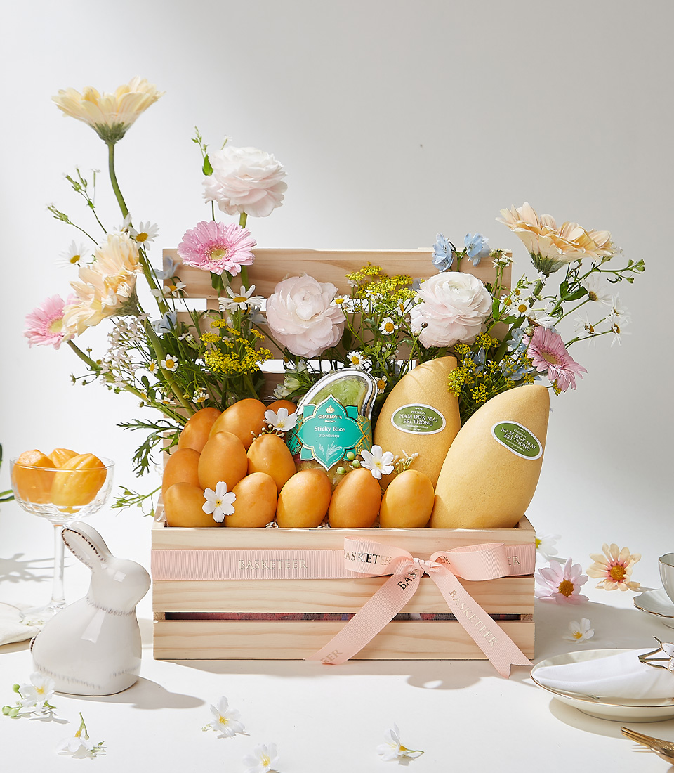 A natural wooden slatted gift box filled with 1 kg of premium Mayongchids from Nakhon Nayok, Nam Dok Mai See Thong mangoes, and Fairy Dust sticky rice, beautifully arranged with fresh flowers and a soft pink ribbon