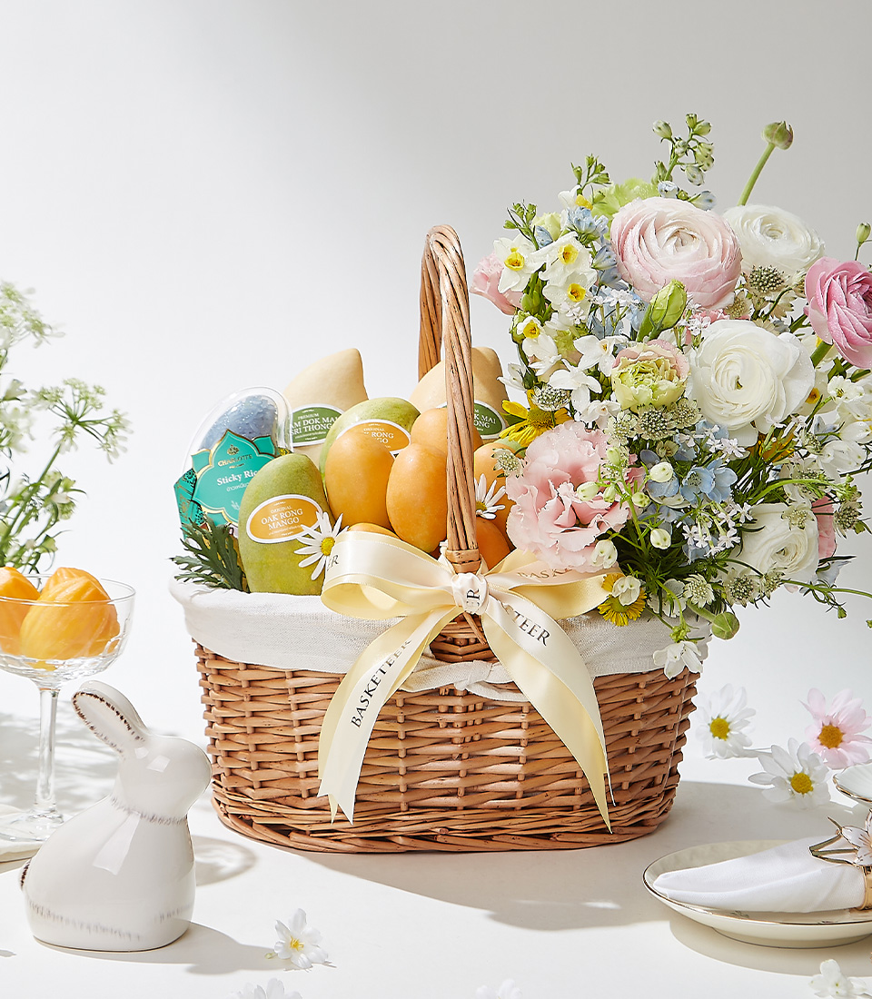 A Classic Grace wicker basket filled with 0.5 kg of premium Mayongchids from Nakhon Nayok, Nam Dok Mai See Thong mangoes, Ok-Rong mango, and Fairy Dust sticky rice, elegantly arranged with fresh flowers and a cream ribbon