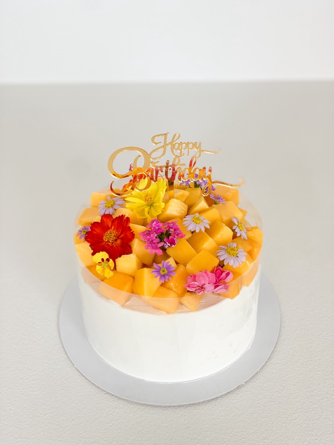 Fresh melon birthday cake topped with vibrant edible flowers and cubes of sweet melon.