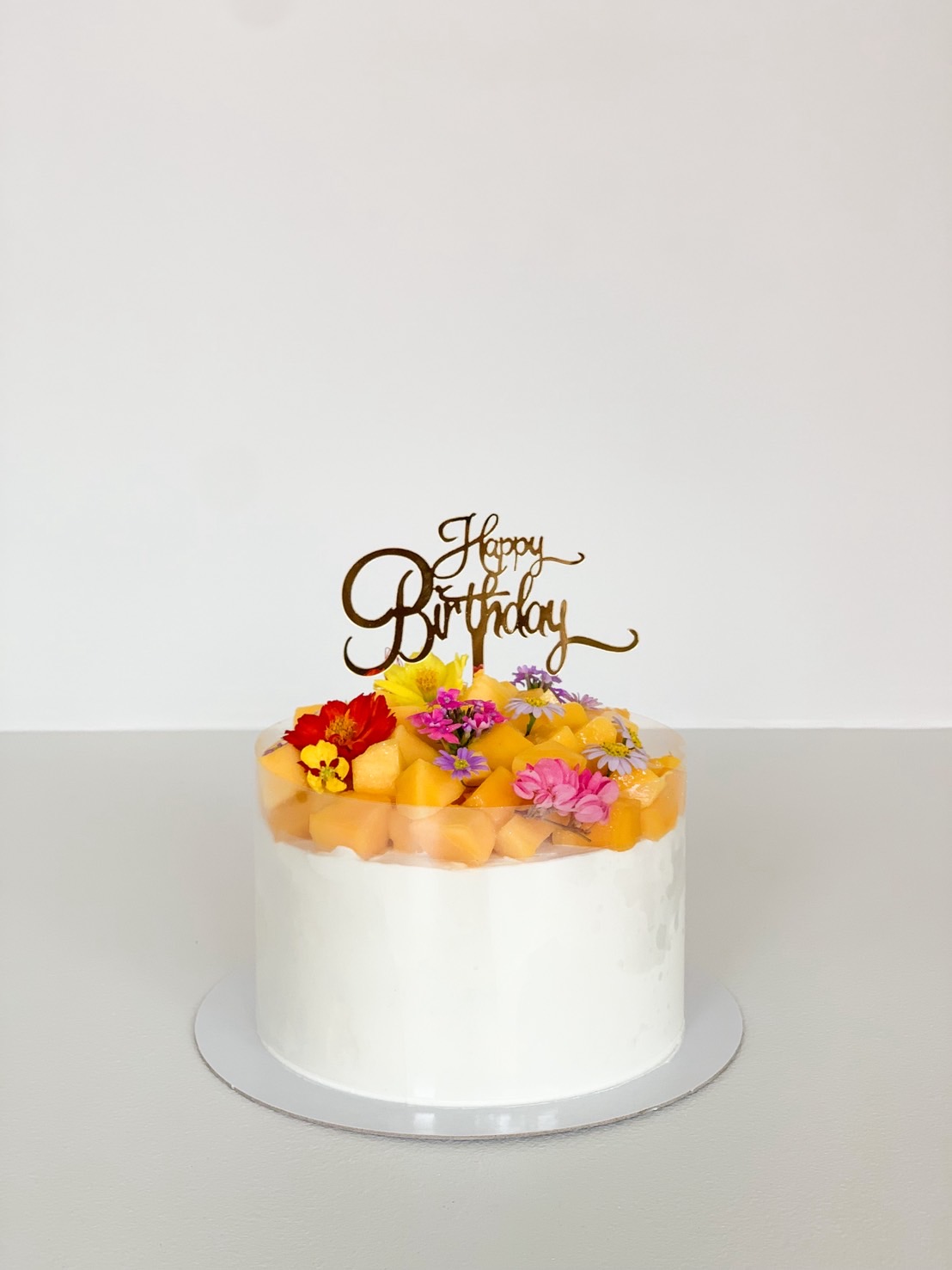 Melon birthday cake topped with golden melon cubes and colourful edible flowers on whipped cream.