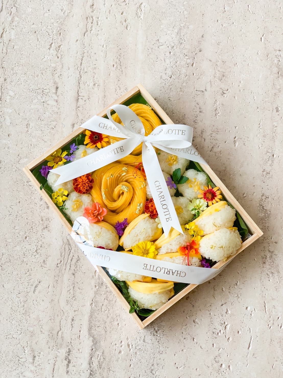 Premium mango sticky rice arranged in a wooden gift box with edible flowers and a white ribbon.