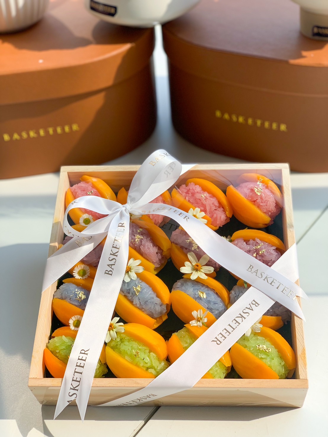 A beautifully arranged gift box of Thai Mayongchid sticky rice in vibrant colors, adorned with delicate edible gold flakes and flowers.