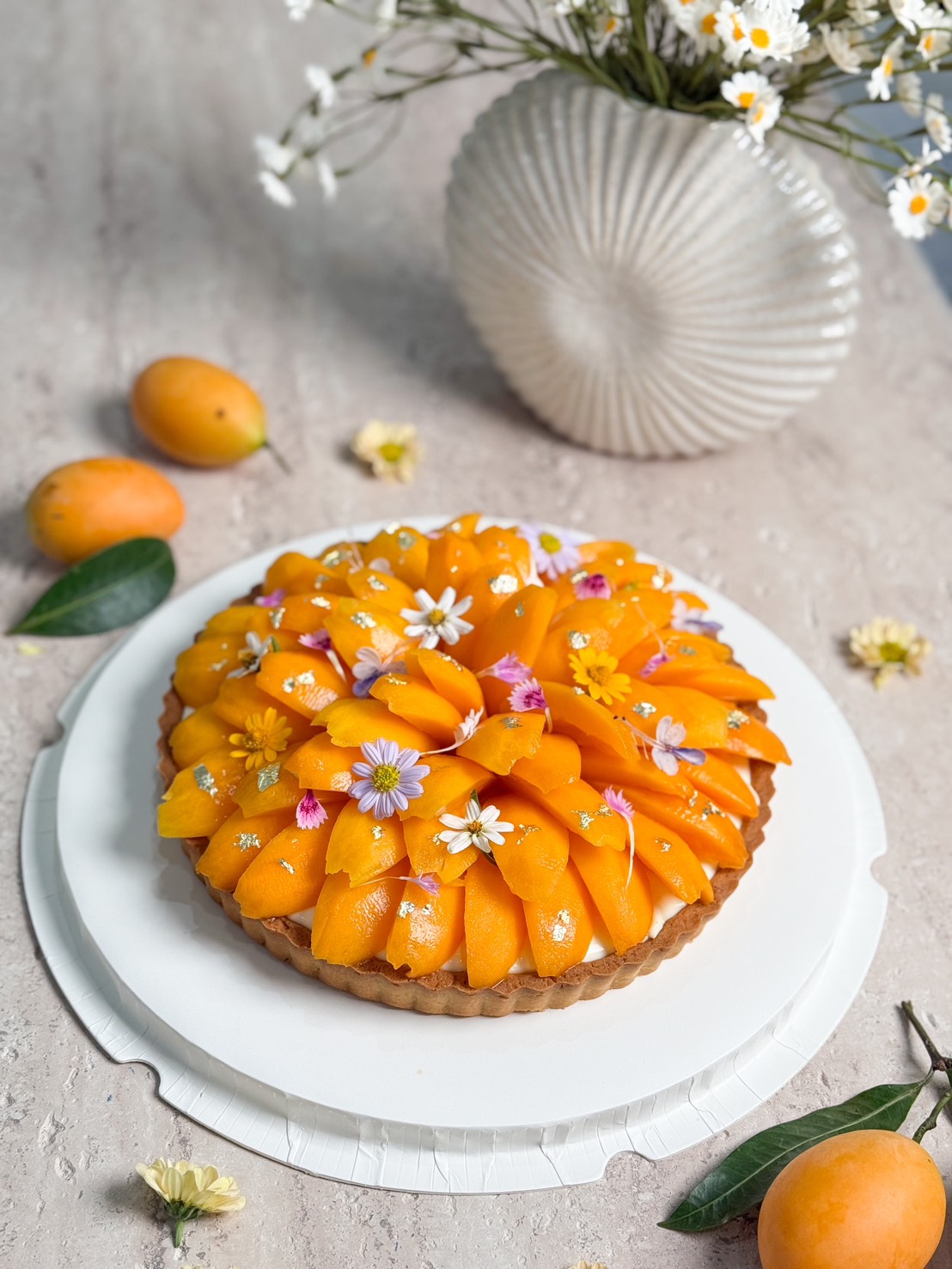 Tropical fruit tart topped with golden marian plums and edible flowers, perfect for special celebrations.