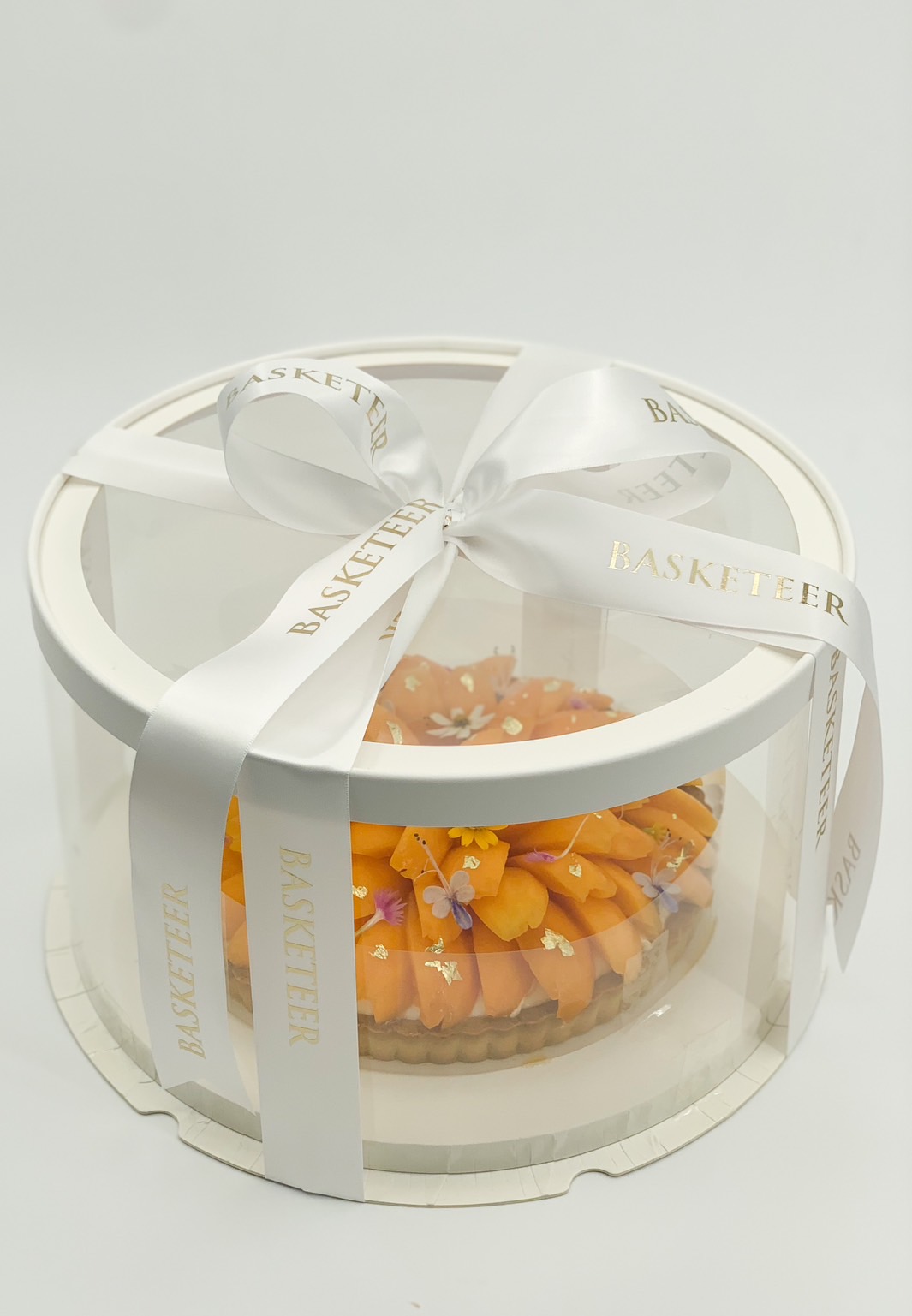 Tropical marian plum tart in a clear gift box with white ribbon and gold foil details.