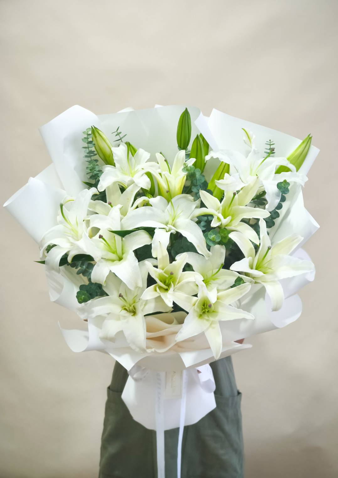 Elegant bouquet of white lilies with green buds and eucalyptus, wrapped in white paper with ribbon.
