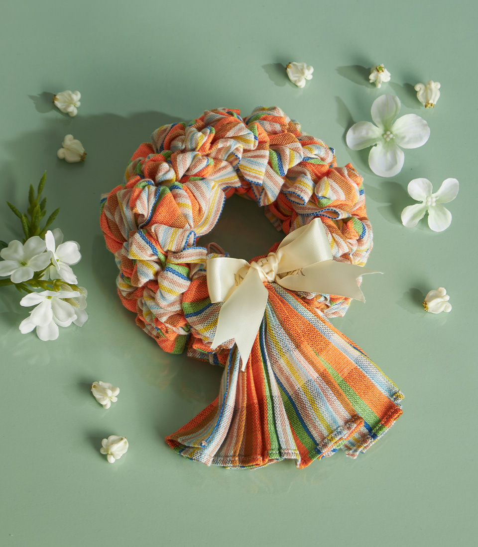 Colourful striped Thai loincloth garland with cream ribbon placed on a green background with white flower petals