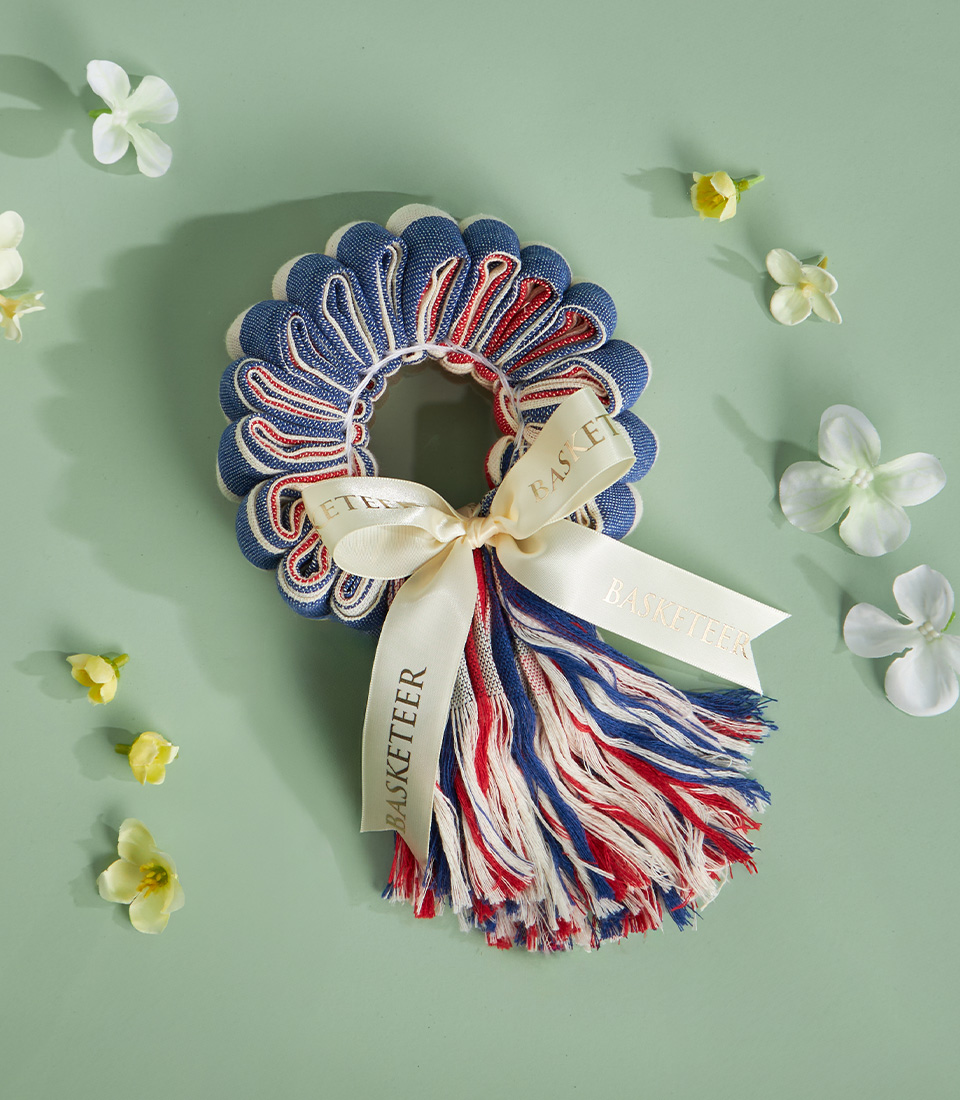 Traditional Thai loincloth garland in red, white, and blue with cream ribbon, placed on a green background