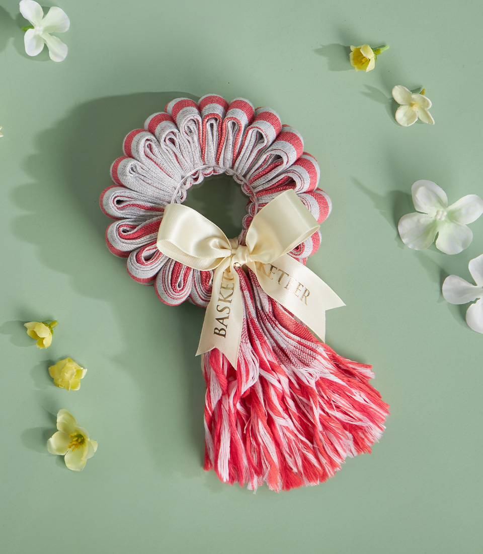 Pink and red Thai loincloth garland tied with ivory satin ribbon, placed on a soft green background with flower petals