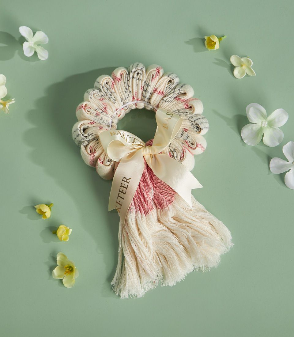 Natural-tone Thai loincloth garland with ivory fringe and ribbon on green backdrop with white floral accents